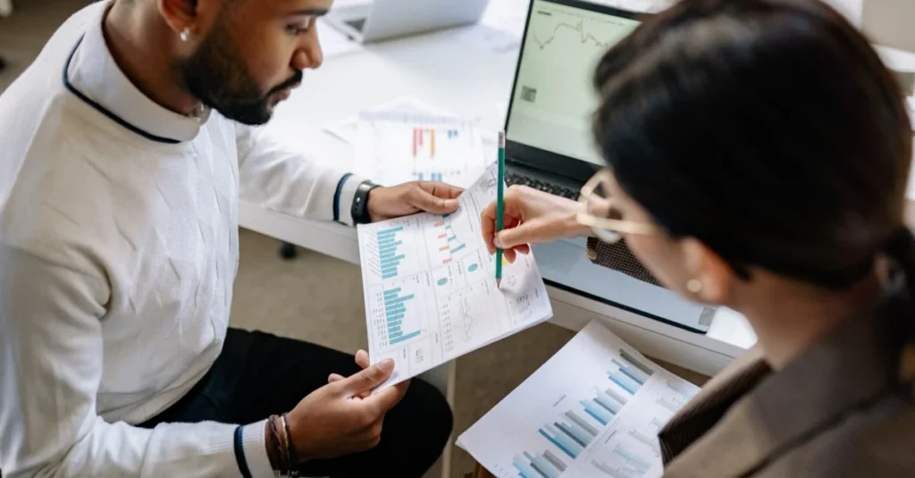 Two professionals reviewing AI tools ecommerce performance charts and analytics on documents at workspace desk.