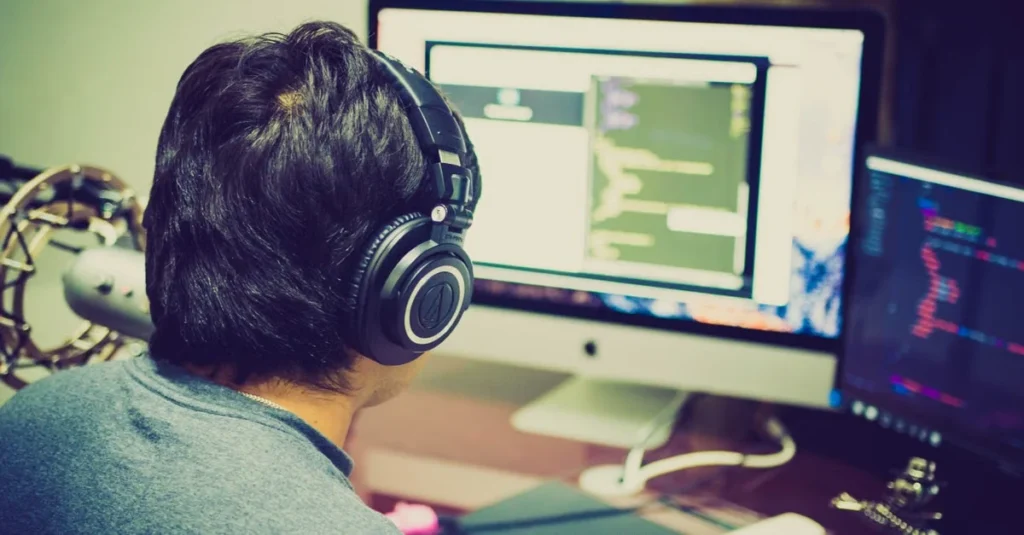 Developer wearing headphones working on ecommerce personalized search interface with code on multiple screens.