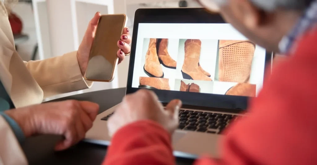 Two people reviewing boot styles on laptop screen during ecommerce product discovery discussion at table.